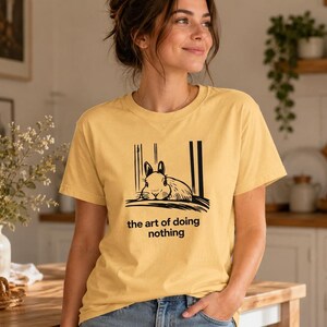 Puede incluir: Una camiseta amarilla de manga corta con un gr&aacute;fico negro de un conejo descansando y el texto "the art of doing nothing" impreso debajo de la ilustraci&oacute;n. La camiseta tiene cuello redondo y un corte relajado en tela de algod&oacute;n lisa.