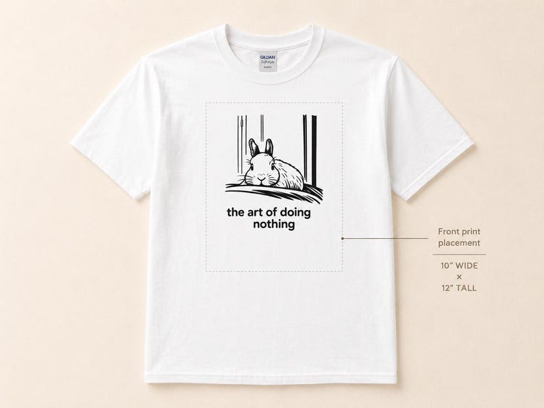 Puede incluir: Una camiseta blanca de manga corta con un gr&aacute;fico negro de un conejo descansando y el texto "the art of doing nothing". Un diagrama indica que el &aacute;rea de impresi&oacute;n frontal mide 25,4 cm de ancho por 30,48 cm de alto.