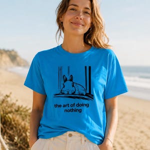 Puede incluir: Una camiseta de manga corta de color azul brillante con un gr&aacute;fico negro de un conejo descansando y el texto "the art of doing nothing" impreso en la parte delantera. La prenda cuenta con cuello redondo y un corte est&aacute;ndar sencillo.