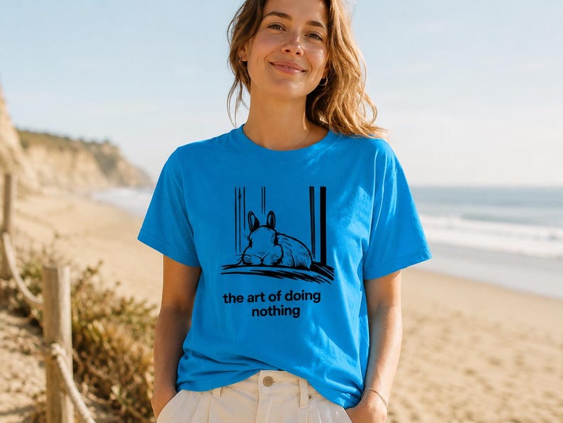 Puede incluir: Una camiseta de manga corta de color azul brillante con un gr&aacute;fico negro de un conejo descansando y el texto "the art of doing nothing" impreso en la parte delantera. La prenda cuenta con cuello redondo y un corte est&aacute;ndar sencillo.