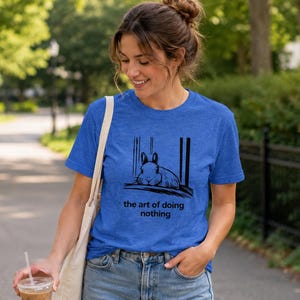 Puede incluir: Una camiseta de manga corta en azul jaspeado con un gr&aacute;fico negro de un conejo descansando y el texto "the art of doing nothing" impreso en la parte delantera. La prenda tiene cuello redondo y corte est&aacute;ndar, acompa&ntilde;ada de una bolsa de tela.