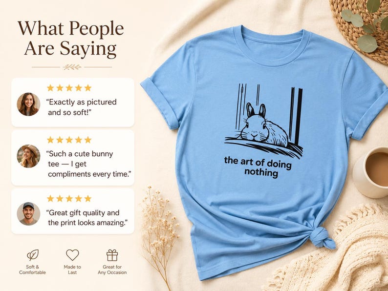 Puede incluir: Una camiseta de manga corta de color azul claro con un gr&aacute;fico negro de un conejo descansando y el texto "the art of doing nothing" impreso debajo. La camiseta se muestra junto a tres rese&ntilde;as de clientes y valoraciones de cinco estrellas.