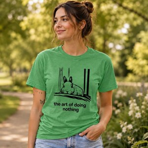 Puede incluir: Una camiseta de manga corta en color verde jaspeado con una ilustraci&oacute;n gr&aacute;fica negra de un conejo descansando sobre una superficie. Debajo del conejo, el texto dice, the art of doing nothing. La camiseta tiene cuello redondo y corte est&aacute;ndar.