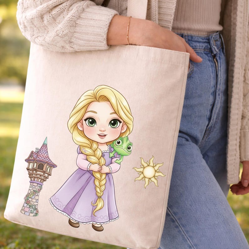 Op de afbeelding: Een beige canvas draagtas met een cartoonillustratie van een blond personage met een lange vlecht in een paarse jurk, die een kleine groene hagedis vasthoudt, met een hoge stenen toren en een gouden zon-symbool.