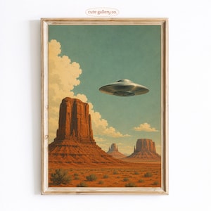 May include: A framed art print featuring a desert landscape with red rock mesas under a teal sky with white clouds. A metallic, disc-shaped UFO hovers in the sky above the rock formations. The text "cute gallery co." is printed at the top centre.