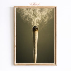 May include: A framed vertical wall art print featuring a lit, cone-shaped rolled cigarette centered against a dark, muted olive-green background. Wisps of white smoke rise from the glowing, charred ember at the top of the paper-wrapped cylinder.