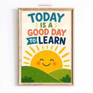 May include: A framed wall art print featuring the text TODAY IS A GOOD DAY TO LEARN in blue, green, and orange lettering. Below the text is a yellow sun with a smiling face rising over green rolling hills with small bushes under a cream background.