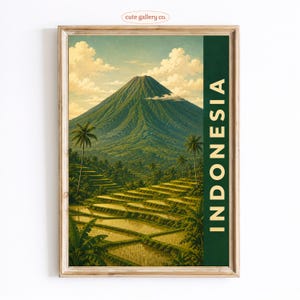 May include: A framed vertical art print featuring a lush green mountain landscape with terraced rice paddies in the foreground and palm trees under a cloudy sky. The word INDONESIA is printed in large, vertical, light-coloured capital letters.