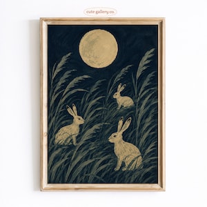May include: A framed art print featuring three light-colored rabbits sitting in tall, dark green grass under a large, pale yellow full moon against a dark navy blue night sky. The text "cute gallery co." is printed in small letters at the top center.