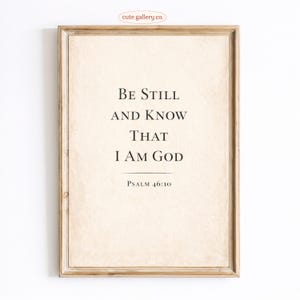 May include: A framed print with the text "Be Still And Know That I Am God" from Psalm 46:10. The text is in a classic serif font on a cream-colored background. The frame is a light brown color.
