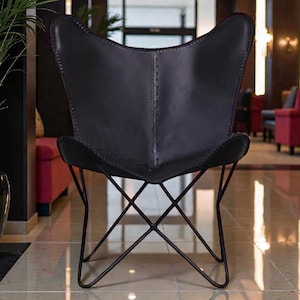 May include: A black leather butterfly chair with a distinctive wing-shaped backrest. The chair features a black metal frame with an X-shaped base. The stitching on the leather is visible, adding to the chair's unique design. This chair is a stylish piece of furniture.