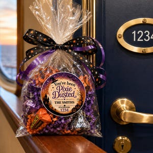 May include: A clear plastic gift bag filled with purple and orange paper shreds and assorted candies. The bag is tied with a black ribbon featuring orange stars and purple edges. A circular label reads: You've been Pixie Dusted, THE SMITHS, 1234.