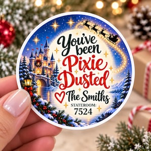 May include: A round sticker featuring a winter castle scene with a snowy landscape, a glowing moon, and Santa's sleigh. The text reads: You've been Pixie Dusted, The Smiths, and STATEROOM: 7524, accented with gold stars and a red heart.