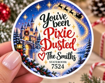 May include: A round sticker featuring a winter scene with a castle, snow-covered trees, and a silhouette of Santa in a sleigh. The text reads: You've been Pixie Dusted, The Smiths, and STATEROOM: 7524, accented with gold stars and a red heart.