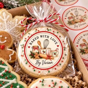May include: A round sugar biscuit in a clear plastic bag tied with red and white twine. The biscuit features a printed label with the text BAKED WITH LOVE By Vivian, showing illustrations of a whisk, rolling pin, jar, and gingerbread man.