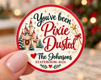 May include: A round sticker with a red border featuring a castle, a gold star wand, and the text "You've been Pixie Dusted", "The Johnsons", and "STATEROOM: 8124". The design includes green pine trees, red hearts, and gold sparkles on a cream background.