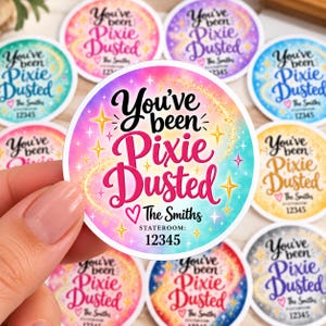 May include: A circular sticker with a gradient background of pink, blue, and yellow. The text reads You've been Pixie Dusted, The Smiths, and STATEROOM: 12345. The design features yellow star icons and a gold glitter trail across the center.