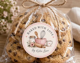 May include: A clear plastic bag tied with twine containing chocolate chip cookies. A round sticker on the front features a pink mixing bowl, whisk, wooden spoon, rolling pin, and measuring cup with the text Baked With Love By Katie Lane.