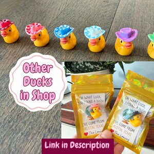 Puede incluir: Una colecci&oacute;n de peque&ntilde;os patos de goma amarillos con sombreros de vaquero en miniatura de varios colores y estampados, junto a dos bolsas doradas selladas que contienen un pato y una tarjeta que dice Oh what luck, you found a duck!