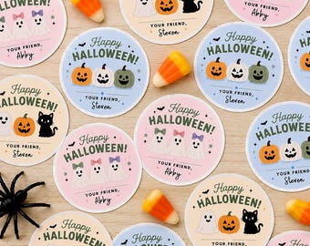 May include: A collection of circular Halloween stickers featuring illustrations of ghosts, pumpkins, and black cats. Each sticker includes the text Happy Halloween and a personalized name like Abby or Steven. Candy corn and a plastic spider are scattered among the stickers.