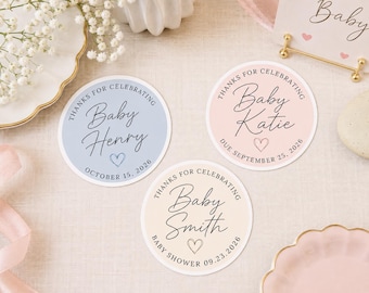 May include: Three circular stickers in light blue, soft pink, and cream. Each features the text "THANKS FOR CELEBRATING" in an arc, a name in script, a hand-drawn heart, and a date. The names are "Baby Henry", "Baby Katie", and "Baby Smith".