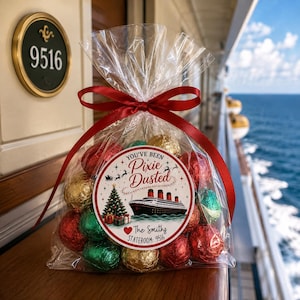 May include: A clear cellophane bag filled with red, green, and gold foil-wrapped chocolates, tied with a red ribbon. A circular label features a cruise ship, a Christmas tree, and the text: You've Been Pixie Dusted, The Smiths, Stateroom: 9516.