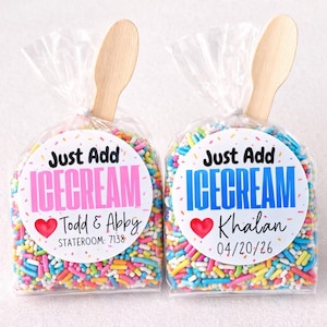 May include: Two clear cellophane bags filled with colorful sprinkles, each topped with a wooden spoon. The bags have circular labels that read "Just Add ICE CREAM" with names and dates. One label is pink, the other blue.