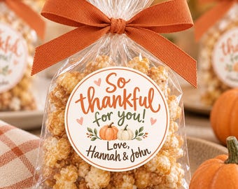 May include: A clear plastic bag filled with caramel popcorn, tied with a burnt orange ribbon. A circular sticker on the front reads: So thankful for you! Love, Hannah & John, featuring illustrations of a small orange pumpkin and a white pumpkin.