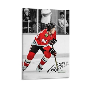 May include: A canvas print featuring a hockey player in a red jersey with the number 98, black shorts, and white socks. The player is skating on the ice with a hockey stick. The background is black and white, with a signature.