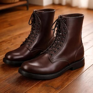 May include: A pair of brown leather lace-up boots with black soles. The boots have a polished finish and are displayed on a wooden surface. The boots are a classic style, suitable for various occasions.