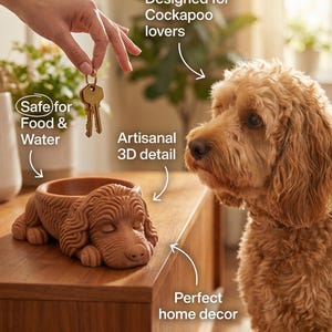 May include: A brown, dog-shaped bowl with artisanal 3D detail, designed for Cockapoo lovers. The bowl is safe for food and water and is placed on a wooden surface. A Cockapoo dog is looking at the bowl.