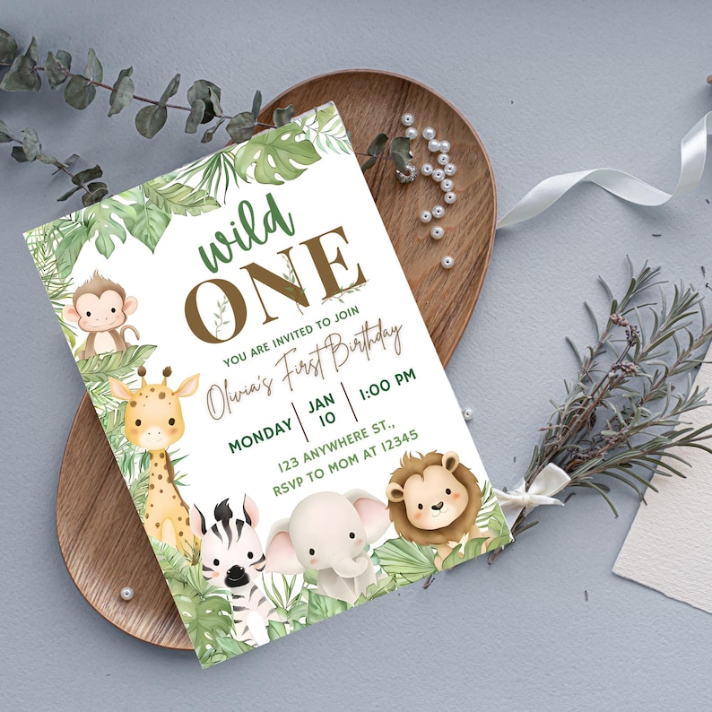 K&ouml;nnte beinhalten: Eine Geburtstagseinladung mit Dschungel-Thema. Die Einladung zeigt den Text "wild ONE" in Gr&uuml;n und Braun sowie "Olivia's First Birthday". Sie ist mit Illustrationen eines Affen, einer Giraffe, eines Zebras, eines Elefanten und eines L&ouml;wen verziert.