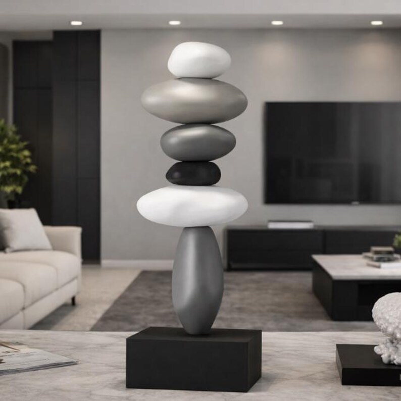 May include: A modern sculpture of stacked, smooth stones in varying shades of gray, white, and black. The sculpture is mounted on a black rectangular base. The artwork is a decorative accent for a living room or similar space.