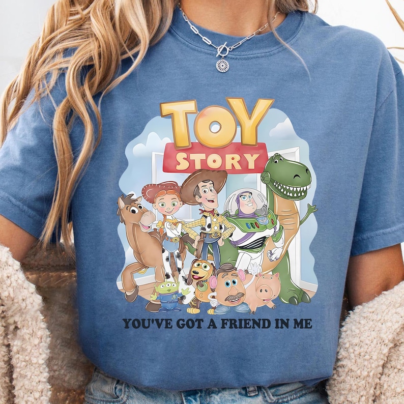 May include: Blue t-shirt featuring a colorful graphic of characters from the animated film "Toy Story." The design includes the words "TOY STORY" and "YOU'VE GOT A FRIEND IN ME."