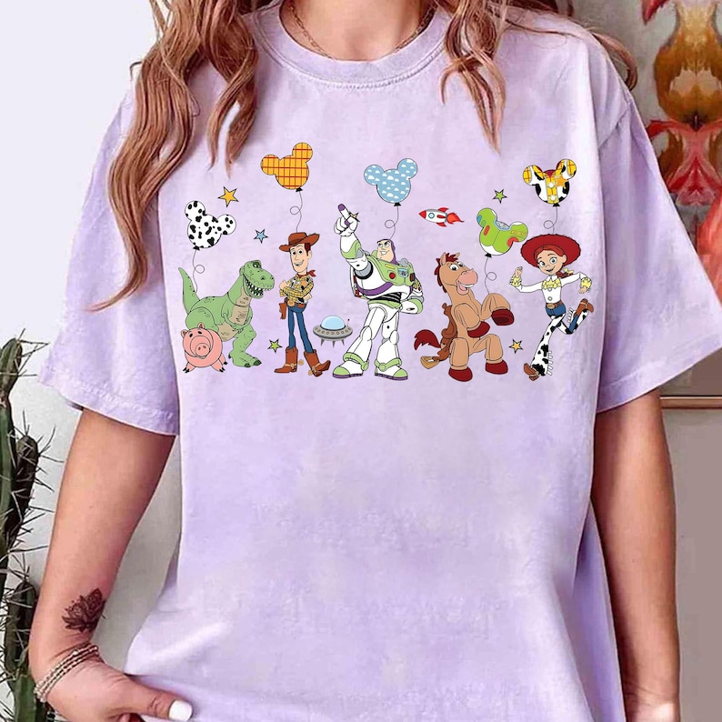 Puede incluir: Una camiseta de color lila claro con un gr&aacute;fico colorido de personajes de Toy Story. El dise&ntilde;o incluye a Woody, Buzz Lightyear y otros personajes, junto con globos y estrellas. La camiseta est&aacute; hecha de un material suave.