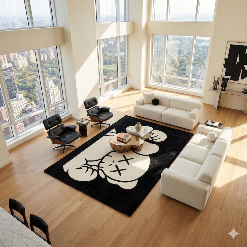 Puede incluir: Una alfombra rectangular grande con fondo negro y un gr&aacute;fico de color crema de un personaje de dibujos animados con ojos en forma de X. La alfombra est&aacute; situada en el centro de una habitaci&oacute;n con suelo de madera clara, dos sof&aacute;s blancos y dos sillas negras.