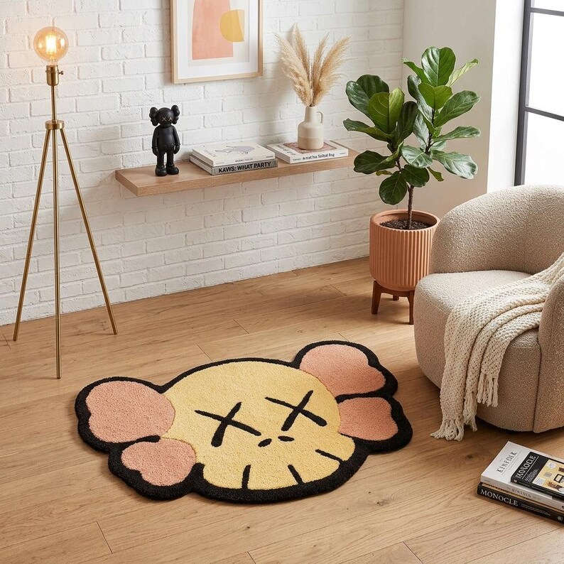 Puede incluir: Una alfombra de pelo insertado con un rostro de personaje estilizado, con un centro amarillo p&aacute;lido, formas de orejas rosa claro y contornos negros gruesos. El dise&ntilde;o incluye dos s&iacute;mbolos X negros para los ojos y una l&iacute;nea de boca negra.