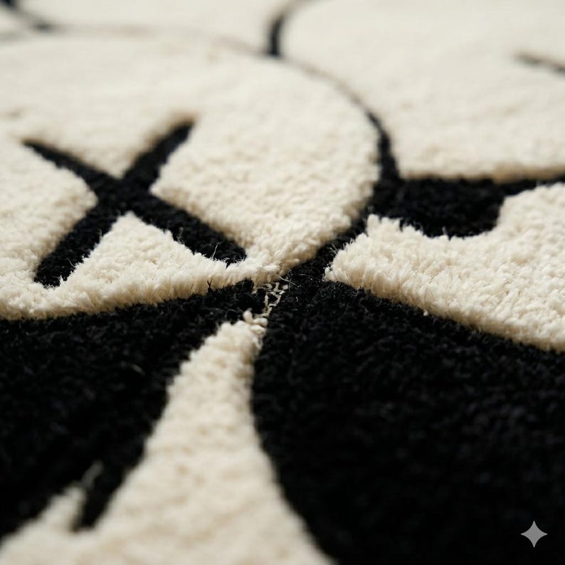 Puede incluir: Una alfombra de mechones con un dise&ntilde;o gr&aacute;fico de alto contraste en crema y negro. La superficie muestra un rostro de personaje estilizado con ojos en forma de X y rasgos redondeados, realizados en un pelo grueso y texturizado con l&iacute;neas limpias.