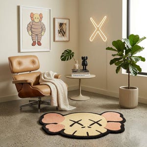 Puede incluir: Un sill&oacute;n de cuero beige con una manta blanca, una mesa redonda con libros y una figura negra, una luz de ne&oacute;n en forma de X, dos cuadros, una planta en maceta y una alfombra beige con forma de cabeza de personaje con ojos en forma de X.