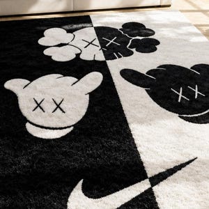 May include: A rectangular area rug featuring a split black and white design. The rug displays cartoon-style gloved hands with X-shaped eyes and a large swoosh logo. The surface has a thick, shaggy texture, contrasting the dark and light sections.
