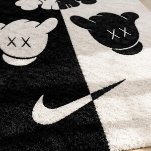 May include: A rectangular area rug featuring a split black and white design. The rug displays cartoon-style character heads with X-shaped eyes and a prominent white Nike swoosh logo. The texture is shaggy, with high-contrast graphics throughout.