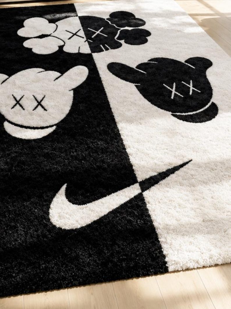 May include: A rectangular area rug featuring a split black and white design. The rug displays cartoon-style character heads with X-shaped eyes and a prominent white Nike swoosh logo. The texture is shaggy, with high-contrast graphics throughout.