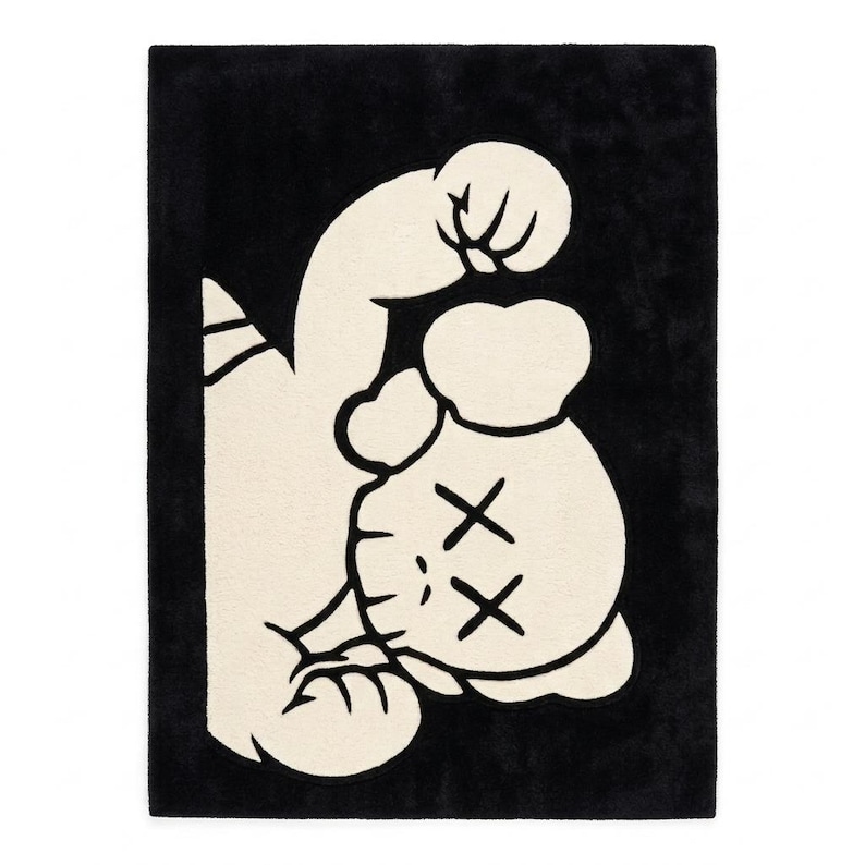 Puede incluir: Una alfombra rectangular con un dise&ntilde;o gr&aacute;fico de alto contraste en negro y blanco roto. La figura central es un personaje estilizado con ojos en forma de X, representado en una pose din&aacute;mica con un brazo levantado sobre un fondo negro.