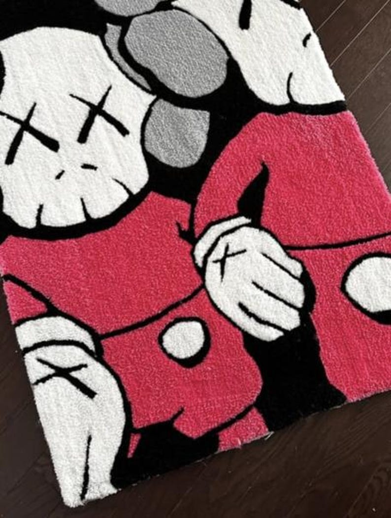 May include: A rectangular tufted rug featuring a graphic design of two cartoon-style figures with white heads, black cross-shaped eyes, and pink bodies. The figures have white gloved hands and are set against a black background with gray accents.