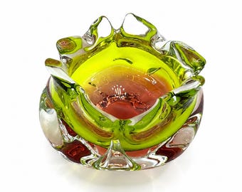 May include: A bowl made of thick, clear glass featuring a vibrant lime green outer layer and a deep orange-red center. The rim has a wavy, organic shape with multiple rounded peaks, and the base is rounded with a smooth, polished finish.
