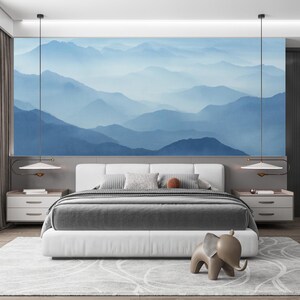 Puede incluir: Un dormitorio moderno con una cama grande con ropa de cama gris y blanca, flanqueada por mesitas de noche blancas. Un mural de montaña azul adorna la pared sobre la cama. Una estatua decorativa de elefante está en el suelo.