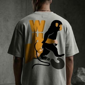May include: Gray t-shirt featuring a black monkey graphic with yellow accents and the text "WH?" in yellow. The monkey is walking towards a question mark. The shirt is a casual, streetwear style.