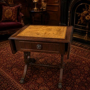 Puede incluir: Una mesa de madera de color marrón oscuro con alas abatibles y una superficie rectangular con incrustaciones de cuero texturizado en tono dorado. Incluye un cajón central con tirador metálico redondo y cuatro patas curvas con garras.