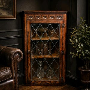 Peut inclure: Un meuble d'angle en bois foncé avec une porte vitrée à motif losange. L'intérieur révèle des livres et de la verrerie. Le bois affiche une teinte chaleureuse, et le meuble est orné de sculptures. Un meuble classique.