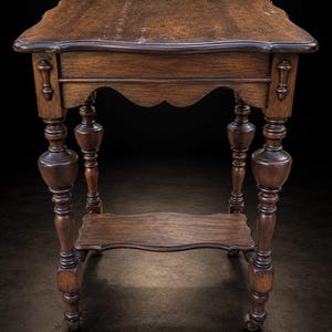 Puede incluir: Una mesa auxiliar de madera marrón oscuro con una superficie rectangular de bordes festoneados, un estante inferior con lados curvos a juego y cuatro patas torneadas con detalles bulbosos. La mesa se apoya sobre pequeñas ruedas giratorias.